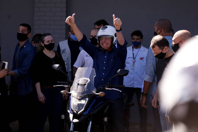 bolsonaro está sentado em garupa de uma moto, com os braços pra cima, e não usa máscara de prevenção  