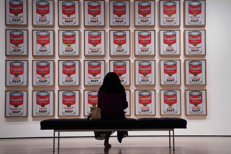 Mulher olhando quadro com várias imagens repetidas de latas vermelha e branca 