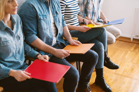 Close up view of young people sitting in chairs with folders before the job interview in the waiting room.