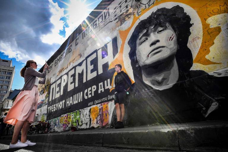 Turistas tiram foto em frente à imagem de Viktor Tsoi em um muro de Moscou 