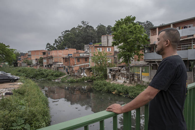 Um homem olhando para um rio poluído cercado de casas inacabadas