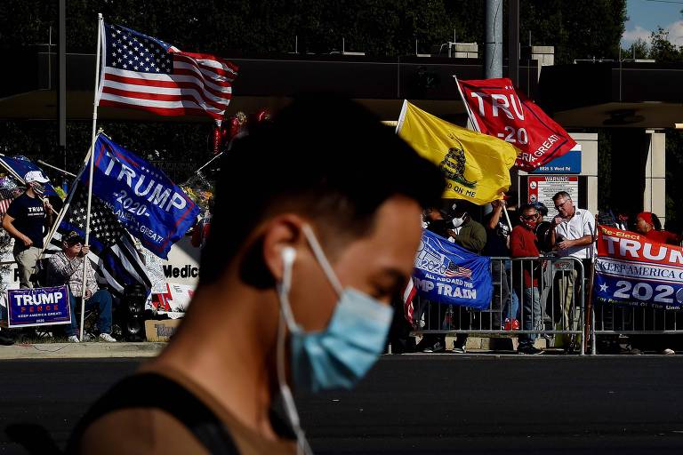 Homem de máscara passa em frente a apoiadores de Donald Trump em frente ao hospital Walter Reed, onde o presidente ficou internado