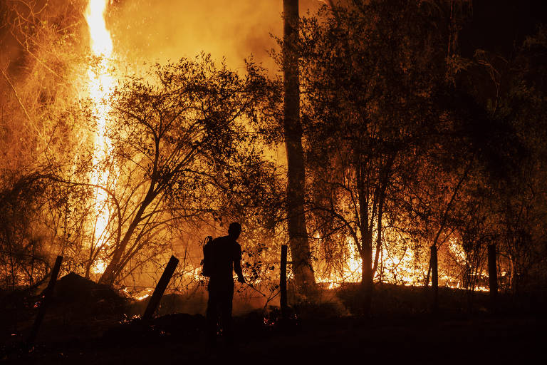 foto escura com tons dourados de homem em meio a incêndio em fazenda 