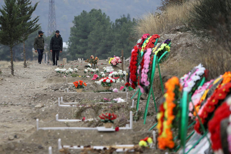 Homens passam por covas recentes com vítimas do conflito entre armênios e azeris em Stepanakert, capital da região de Nagorno-Karabakh
