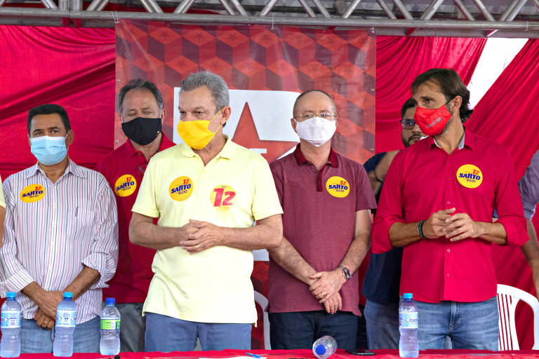 homem de máscara amarela em palanque com outros homens de camisa vermelha