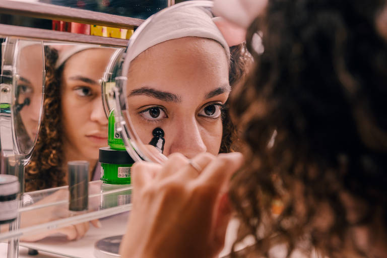 jovem se vê no espelho usando cosméticos