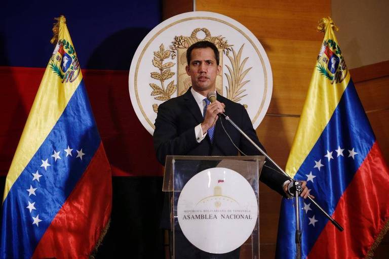 Juan Guaidó, de terno, segura microfone na frente de um púlpito, com duas bandeiras da Venezuela ao fundo