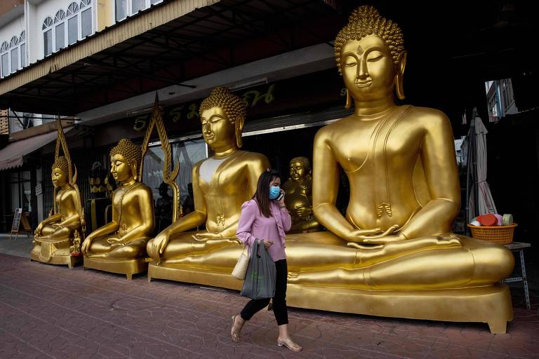 Mulher de máscara passa por imagem de buda em Bangcoc 
