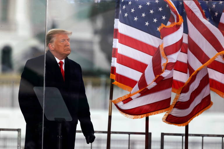 Donald Trump com a bandeira americana flamulando ao seu lado