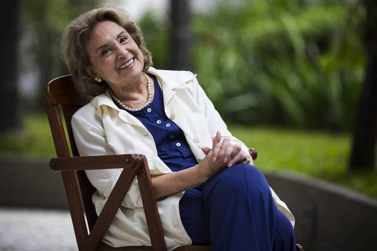 Mulher sentada em cadeira sorrindo para foto.