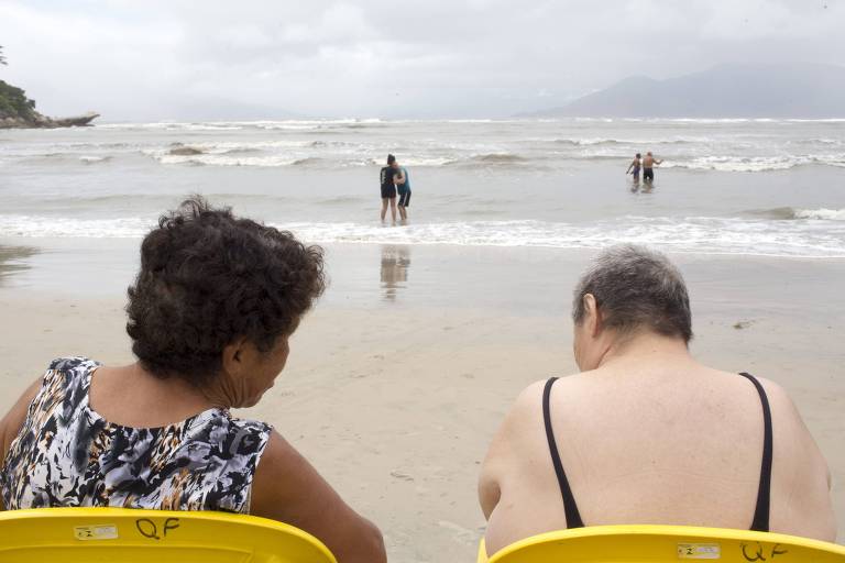 Duas idosas sentadas em cadeiras amarelas de frente para o mar