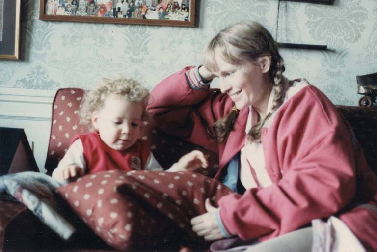 mulher loira sorri para bebê loiro sentado no sofá