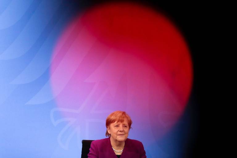 Merkel sentada numa cadeira com uma grande bola vermelha sobre fundo azul atrás