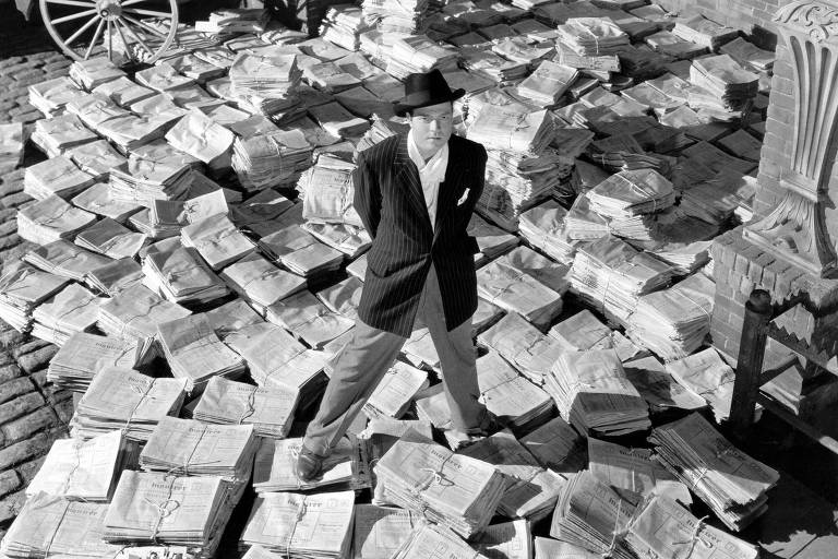 O personagem Charles Foster Kane (Orson Welles) em cima de pilhas do seu jornal, em cena de 'Cidadão Kane' (1941)