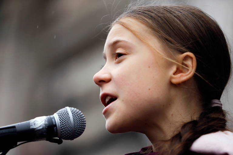 Retrato fechado de Greta Thunberg de perfil, falando num microfone