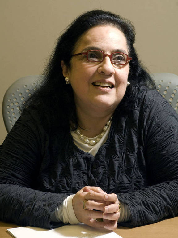 Rosa Freire D'Aguiar sentada com mão cruzada sobre uma mesa