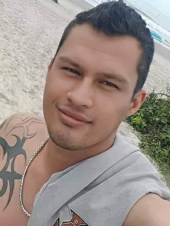 Homem branco tatuado posa em selfie, enquanto está na praia