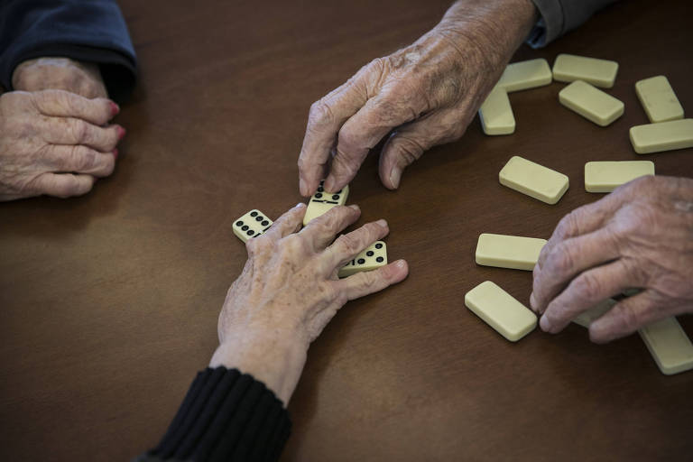 mãos de idosos movimentam peças de dominó 