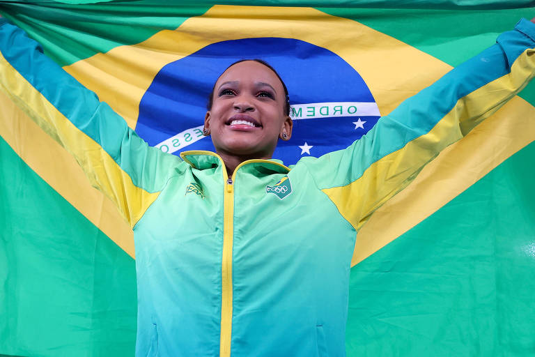 Rebeca Andrade ergue a bandeira do Brasil após conquistar o ouro no salto