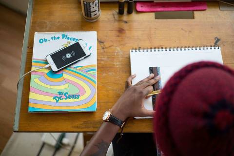 Estágio - Dia do Estagiário - Web Stories - Jovem trabalhando na mesa com caderno, régua e celular carregando