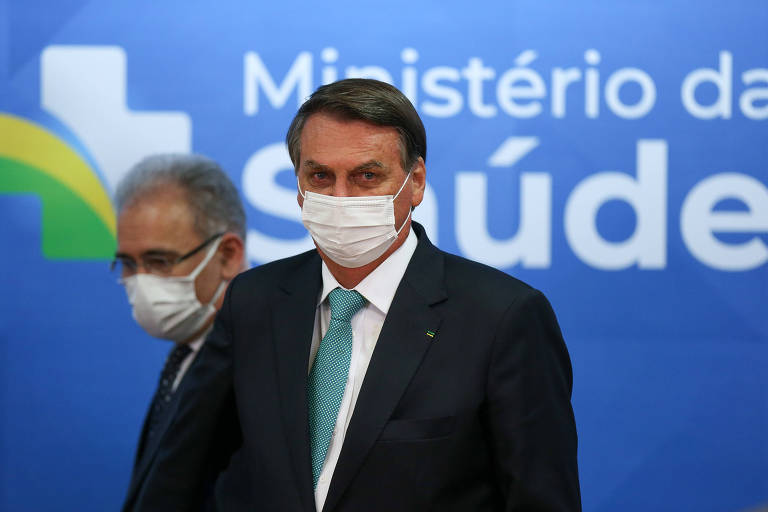 Presidente Jair Bolsonaro em primeiro planto. Marcelo Queiroga, ministro da Saúde, em segundo plano. Ambos aparecem à frente de um banner azul onde se lê "Ministério da Saúde".