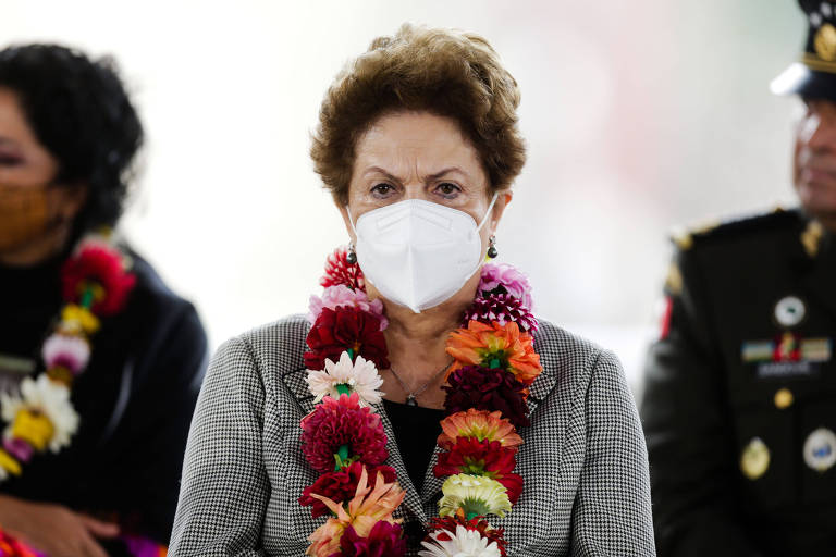 Dilma, com máscara e colar de flores, olha para frente