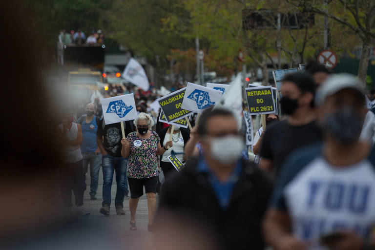 Foto mostra várias pessoas caminhando em uma rua arborizada. Há placas com os dizeres CPP e é possível ver um caminhão de som ao fundo.