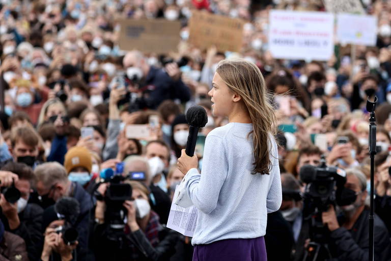De camiseta branca de mangas longas e cabelos soltos, Greta falar para plateia com vários jovens, ao ar livre