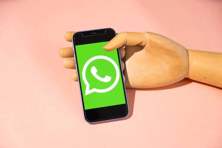 Mão de madeira segura celular com logo do Whatsapp 