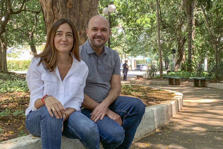 casal de homem e mulher está sentada em beira de calçada de praça bem arborizada