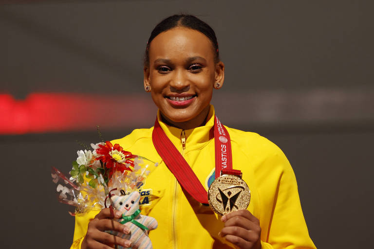 Rebeca, com agalho amarelo, sorri mostrando a medalha de ouro