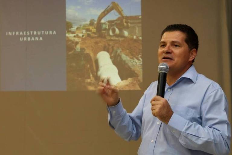 Homem falando em microfone com foto em slide ao fundo