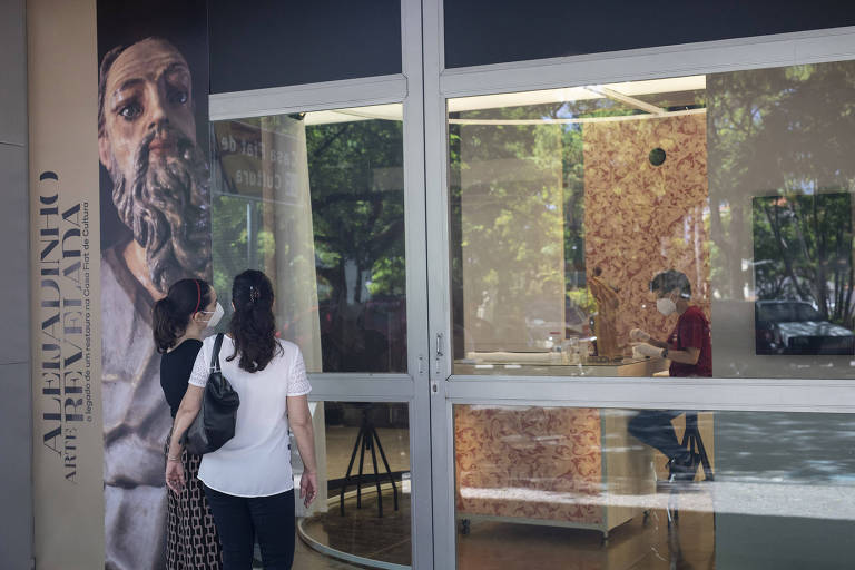 Imagem mostra a fachada de vidro do prédio e duas mulheres observando o trabalho dos restauradores