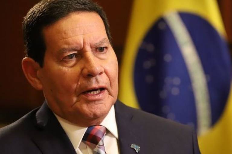 Em destauque, Hamilton Mourão de social. Ao fundo, se vê uma bandeira do Brasil