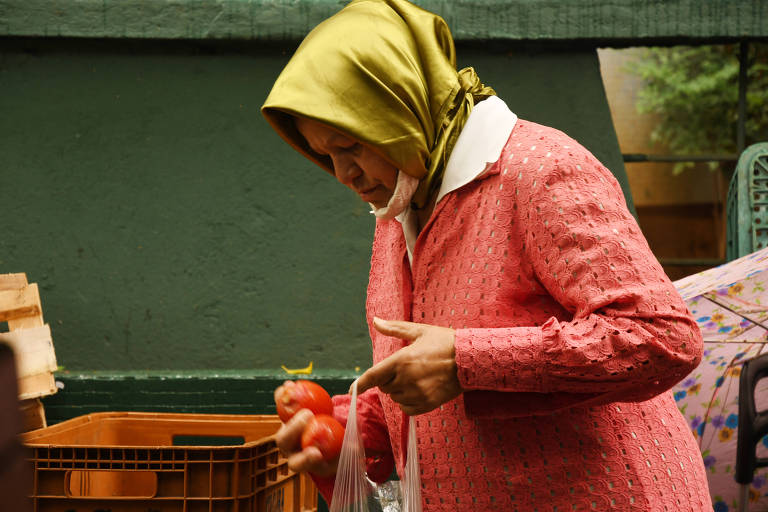 Mulher de lenço na cabeça pega tomate que foi despejado na rua