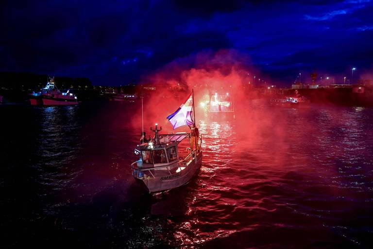 Silhueta de barco é vista contra forte luz vermelha, que reflete nas águas do canal da mancha, na escuridão