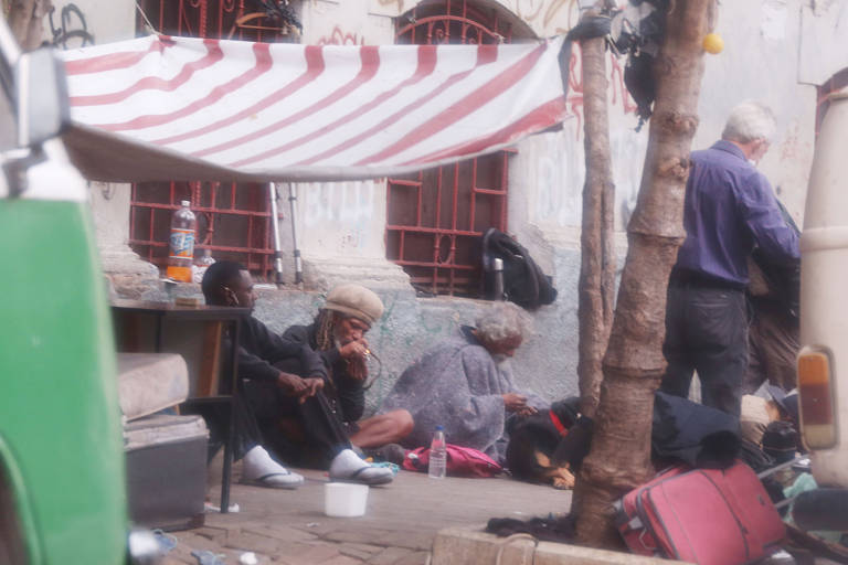 Em uma rua sua, homens estão sentados fumando cachimbos de crack 