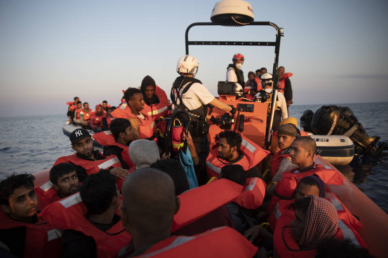Pessoas estão em um barco; elas usam coletes salva-vidas