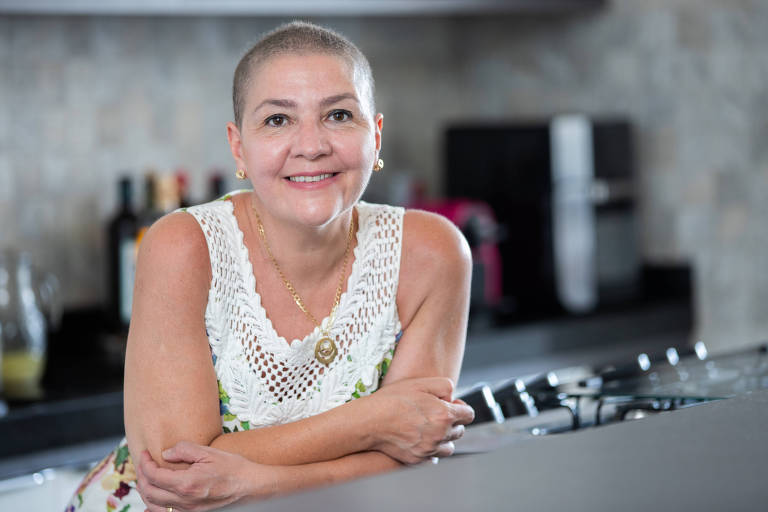 Jackeline Godoni olha para a câmera e sorri; ela veste roupa clara e tem os braços cruzados