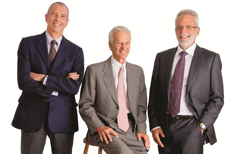 três homens grisalhos, de terno, sorriem