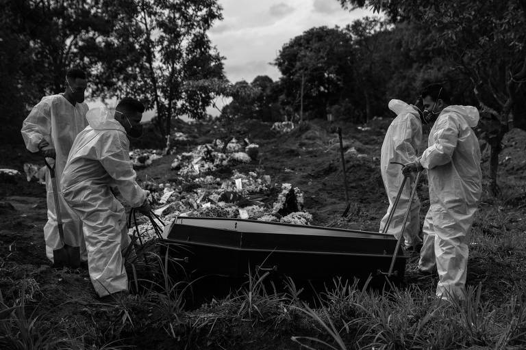 Sepultadores paramentados enterram caixão no Cemitério Vila Formosa, em São Paulo