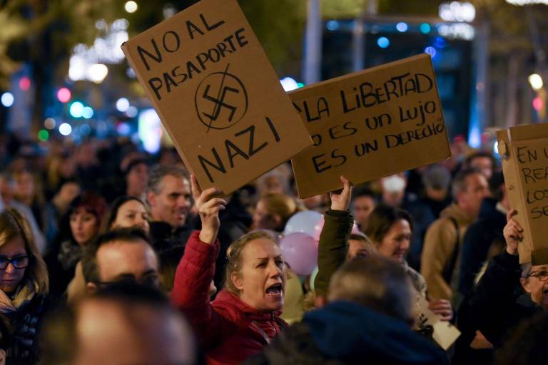 Manifestantes seguram cartazes com os dizeres "liberdade não é luxo, é direito", e "não ao passaporte nazista", durante manifestação contra o passe de saúde Covid-19, em Barcelona