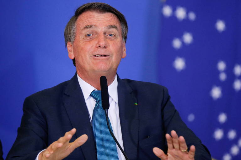 Imagem em primeiro plano mostra o presidente Jair Bolsonaro de social, de frente para um microfone e gesticulando com as mãos.