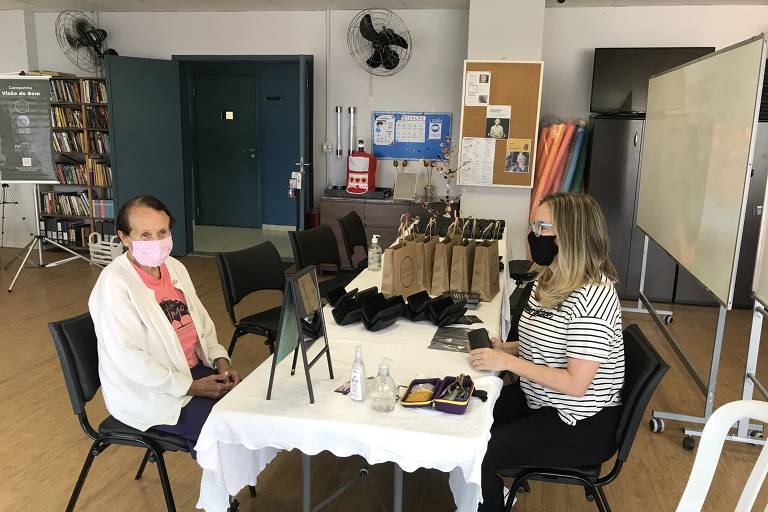 em uma sala ampla, duas mulheres estão sentadas à mesa 