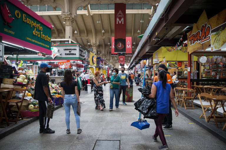 Pessoas caminham em um dos corredores do Mercado Municipal. Ao redor, há barracas