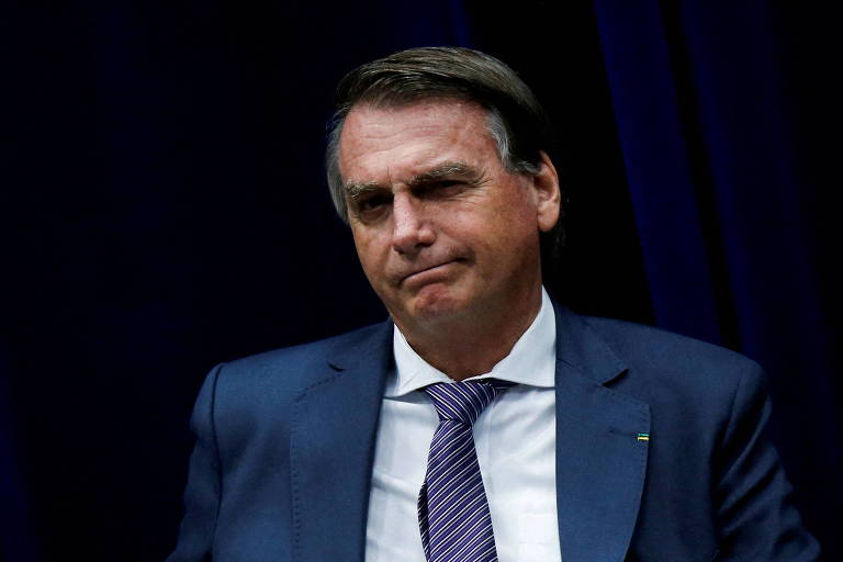 Bolsonaro aparece do peito para cima. Ele veste terno com paletó azul e gravata da mesma cor. É um homem branco e grisalho.