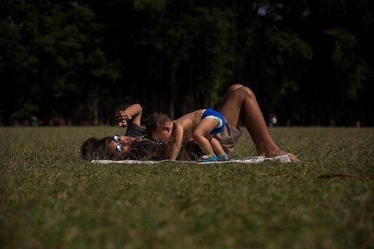 Mãe e filho tomam sol em dia de calor no gramado do parque do Ibirapuera na zona sul de São Paulo