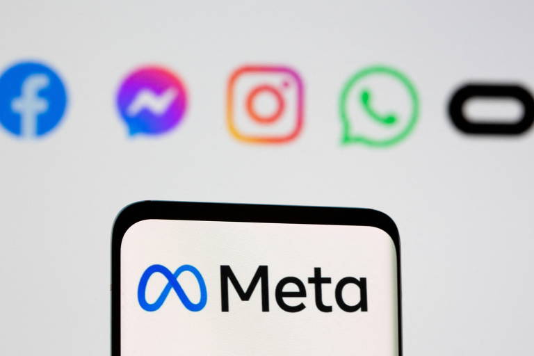 Smartphone mostra logo de Meta em tela branca. Ao fundo, há um banner com logos de Facebook, Messenger, Instagram, WhatsApp e Oculus