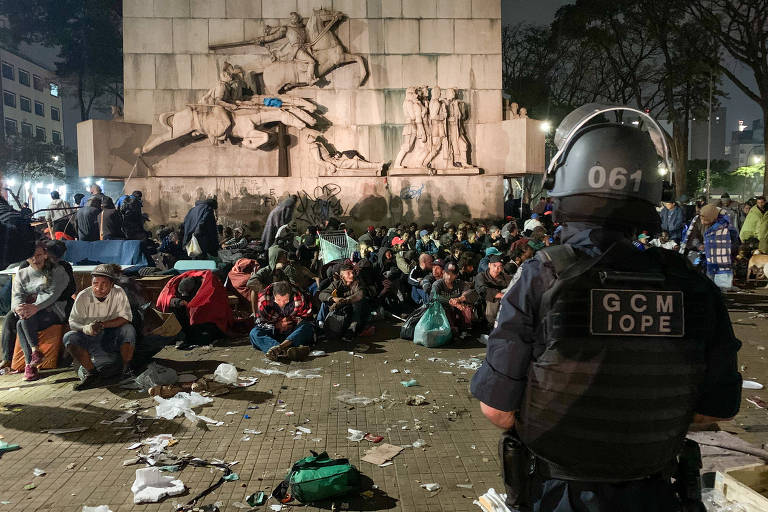 Guarda civil, de costas, observa dependentes químicos agrupados em torno de monumento