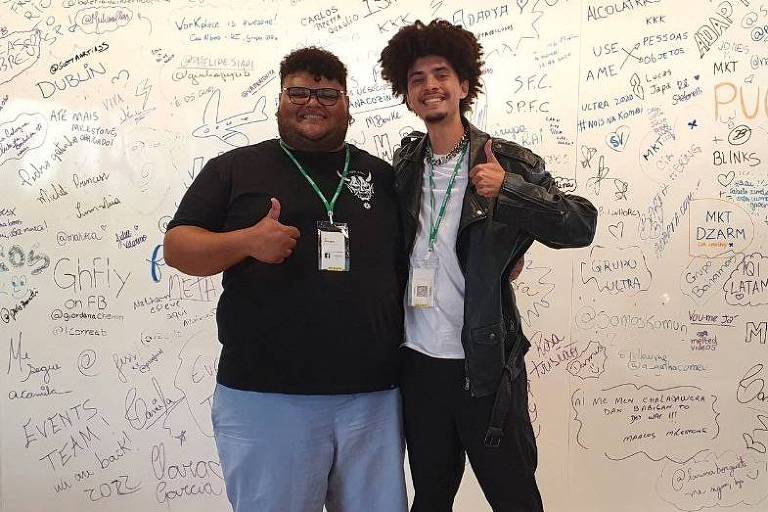 dois rapazes jovens estão abraçados e posando para foto fazendo sinal de joinha com os dedos